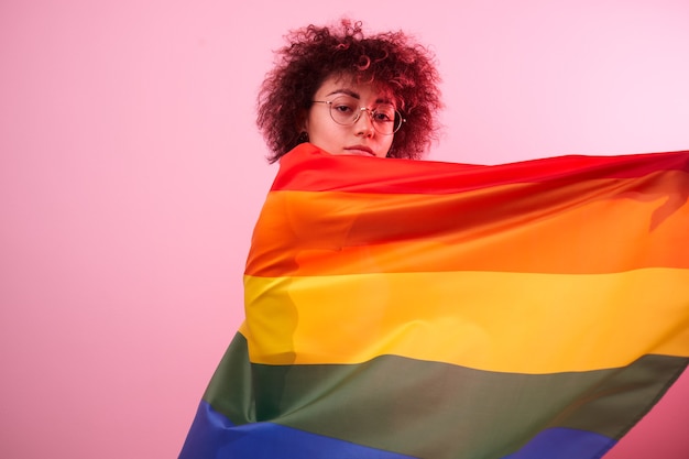 LGBTQ-concept. Positief Kaukasisch meisje dat met afro krullend haar regenboogvlag houdt geïsoleerd