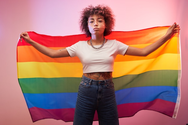 LGBTQ-concept. Positieve Kaukasisch meisje met afro krullend haar met regenboogvlag geïsoleerd in de studio