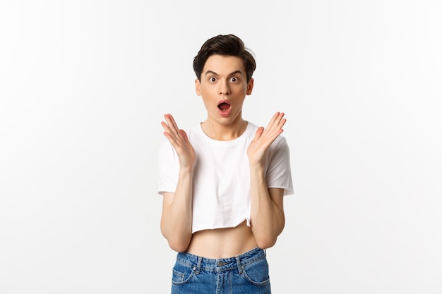 Lgbtq en trots concept. afbeelding van verbaasde queer man klappen in de handen en kijken met ontzag naar de camera, staande in crop top tegen wit.