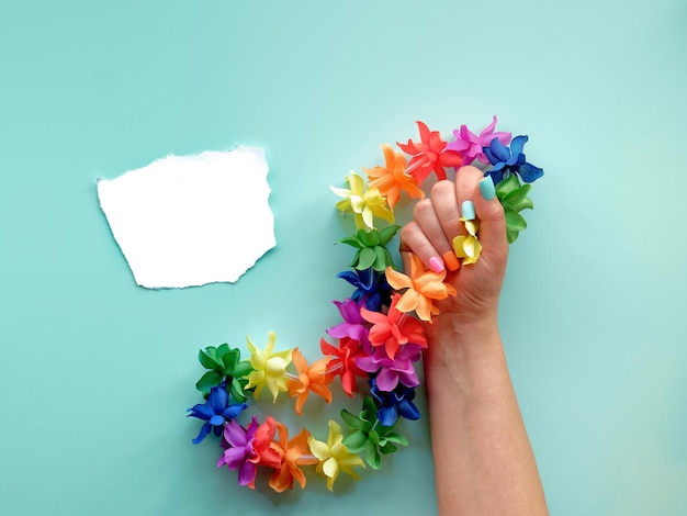 LGBTQ gemeenschap trots maand tekst op papierafval Hand met valse nagels in de kleuren van de regenboog houdt regenboog gekleurde bloemenslinger Plat lag bovenaanzicht op mint groene achtergrond