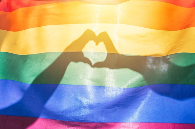 LGBTQ-regenboogkleurenvlag en twee handen die een hartvorm maken die schijnt door zonlicht voor de trotsmaand