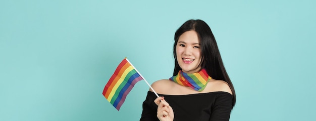 LGBTQ woman holding pride flag standing against a blue green background