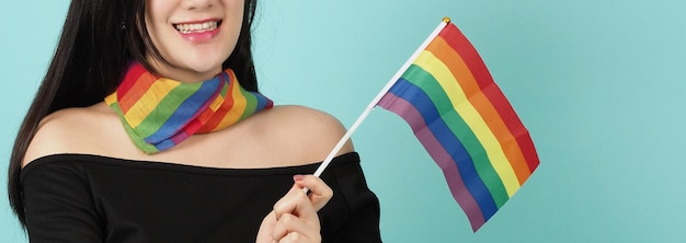 LGBTQ woman holding pride flag standing against a blue green background