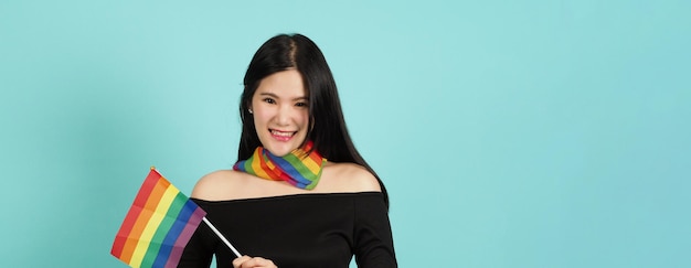 LGBTQ woman holding pride flag standing against a blue green background