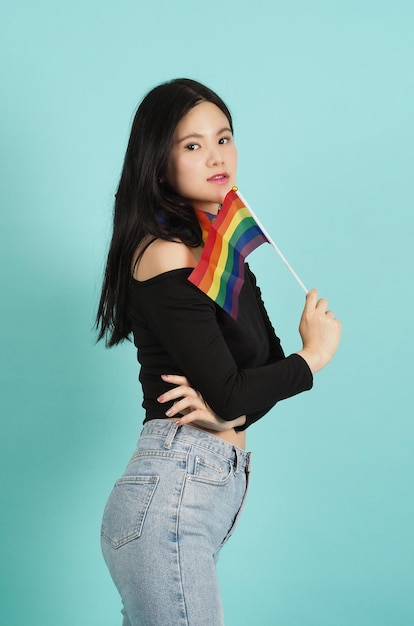 LGBTQ woman holding pride flag standing against a blue green background