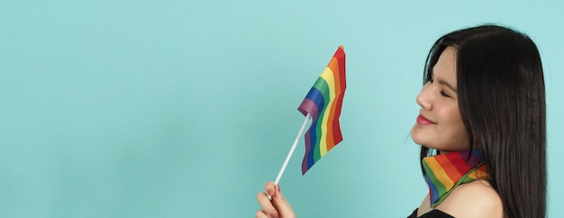 LGBTQ woman holding pride flag standing against a blue green background