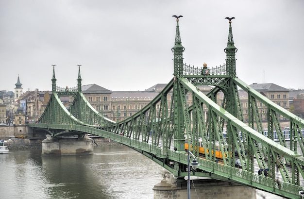 Liberty Bridge in Budapest Hungary with a yellow tram crossing on a cloudy winter day