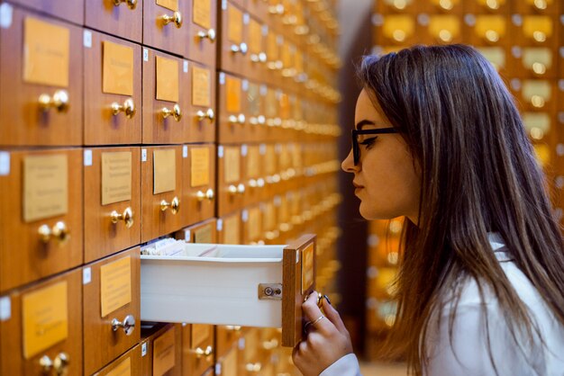 Photo library or archive reference card catalog. student girl trying to find necessary book using library paper database