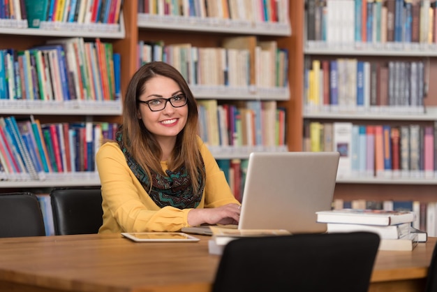 In The Library  Beautiful Female Student With Laptop And Books Working In A High School  University Library  Shallow Depth Of Field