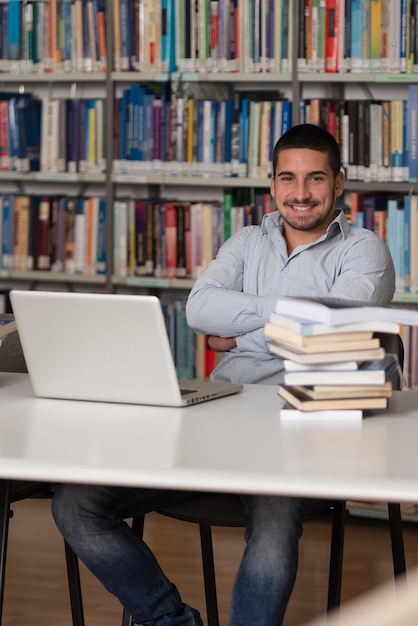 In The Library  Handsome Male Student With Laptop And Books Working In A High School  University Library  Shallow Depth Of Field