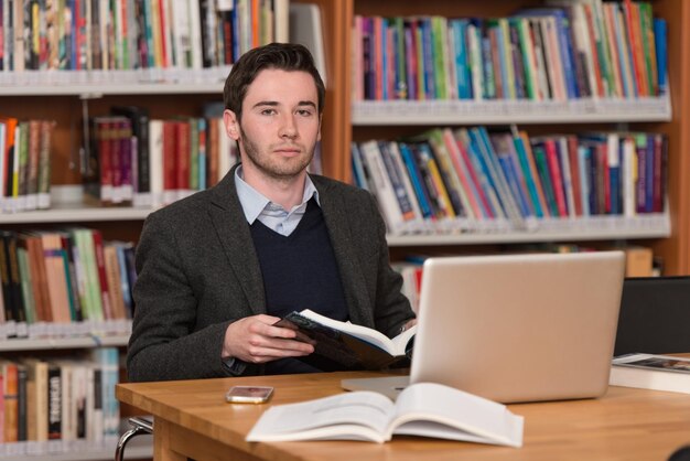 In The Library  Handsome Male Student With Laptop And Books Working In A High School  University Library  Shallow Depth Of Field