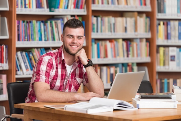 In The Library  Handsome Male Student With Laptop And Books Working In A High School  University Library  Shallow Depth Of Field