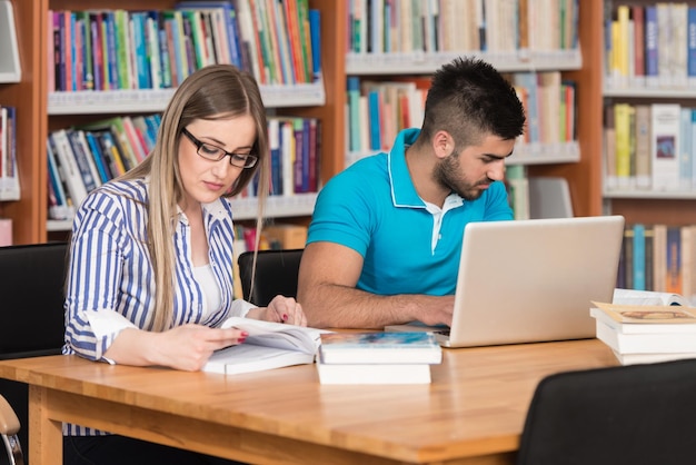 図書館でノートパソコンと本を持ったハンサムな2人の大学生が高校の大学図書館で働いています浅い被写界深度