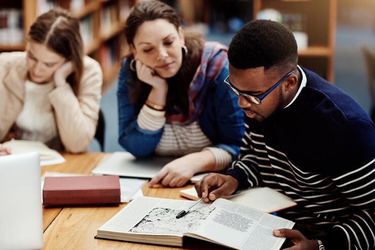 Photo library people and studying with book research and reading for exam woman and man in campus of college students friends and teamwork for test information and table with project and together