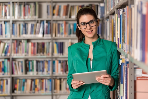 図書館でタブレットと本を持ったかなりの女子学生が高校の大学図書館で働いている浅い被写界深度