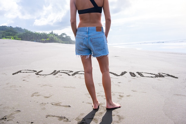 Lichaam van een vrouw in zomerkleren die voor brieven in het zand van een strand staat