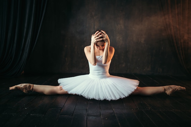 Lichaamsflexibiliteit van balletartiest, rekoefening. ballerina in witte jurk zit op een touw op zwarte houten vloer