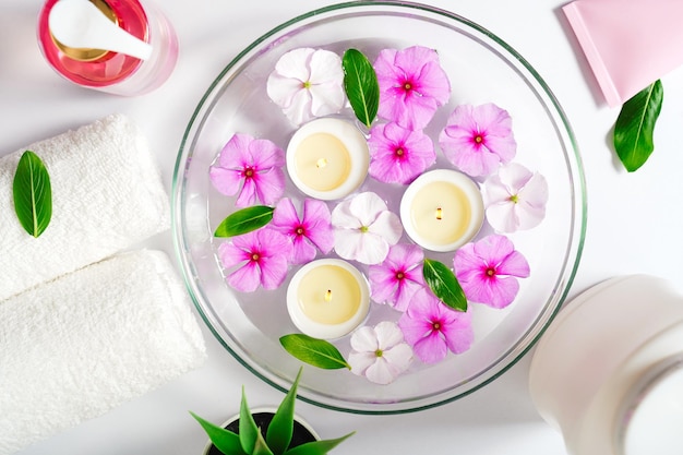 Lichaamsverzorging levert witte handdoekolie en rozenbloemen op een witte achtergrond brandende drijvende kaarsen i...