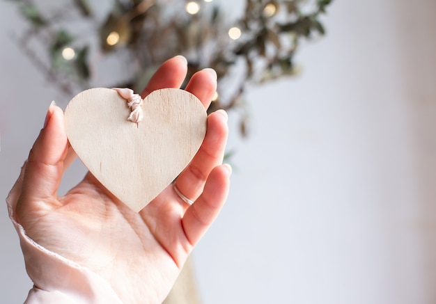 Licht houten hart op een zijden roze lint op witte achtergrond. Ruimte voor tekst. Hand met een houten harthanger aan een lichtroze lint van chiffon. Ruimte kopiëren.