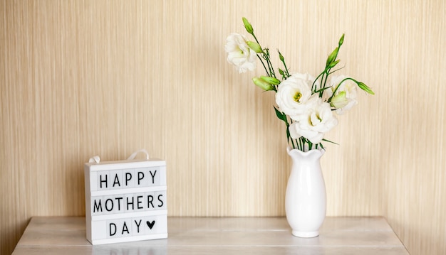 Lichtbak met belettering Happy Mother's Day, witte bloemen Eustoma of Lisianthus in vaas op houten tafel met kopie ruimte.