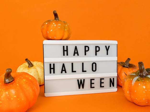 Lichtbak met Happy Halloween-zin met pompoenendecoratie op een oranje achtergrond.