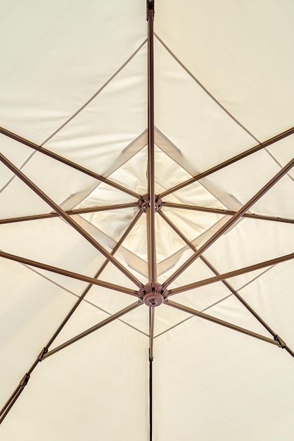 Lichtbeige paraplu beschermt cafébezoekers tegen zonnestralen vanuit een lage hoek