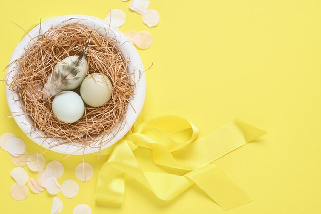 Lichtblauwe paaseieren in nest op gele trendkleur achtergrond. Pasen minimale creatieve horizontale compositie met kopie ruimte. Bovenaanzicht.