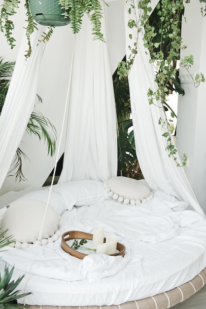 Lichte knusse slaapkamer gemaakt in witte kleuren met rond hemelbed. Moderne gezellige slaapkamer met rond hemelbed en groene tropische planten. Luie ochtend thuis en perfecte plek voor ontspanningsconcept.