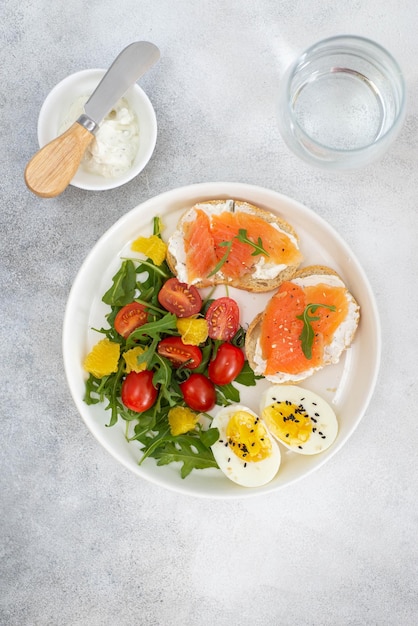 lichte salade van groenten twee zalmsandwiches eieren op wit vlak met glas water