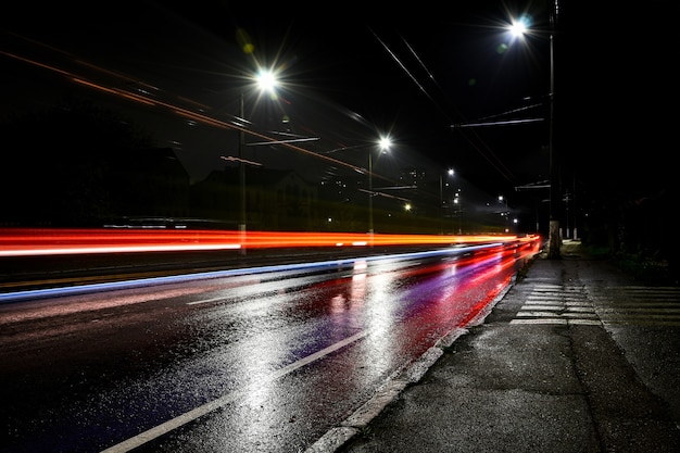 Lichten van auto 's nachts. Straatverlichting. Nacht stad. Lange belichtingsfoto nacht weg. Gekleurde banden van licht op de weg. Natte weg na regen.
