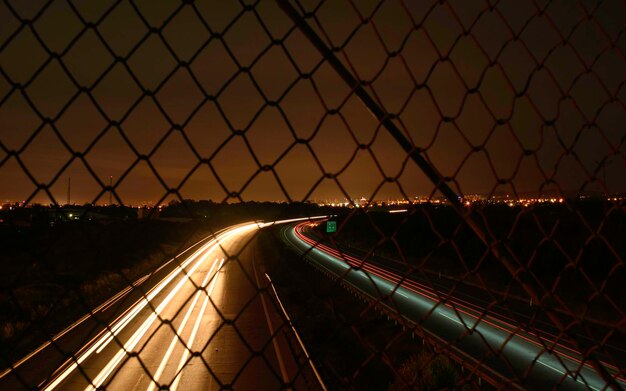 Foto lichtpaden op de snelweg gezien door een kettinghek tegen de hemel 's nachts