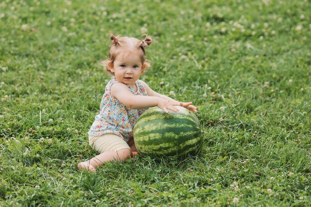 lief babymeisje met een enorme watermeloen zit op een groen gazon kind speelt buitenshuis levensstijl