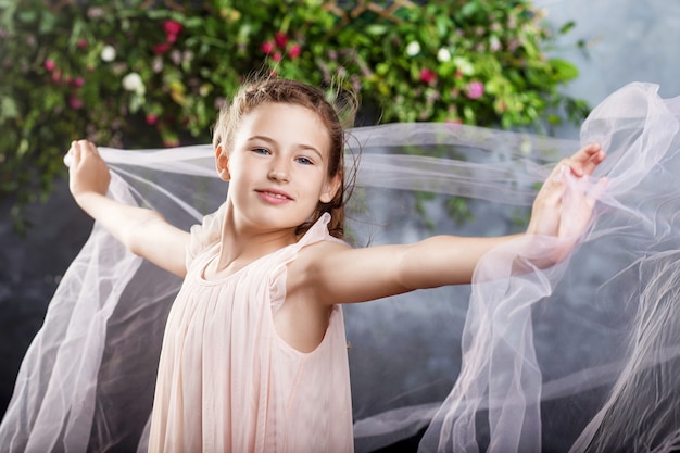 Lief klein meisje speelt met lichte stof tegen de bloemen. Portret van het aardige kleine meisje. Dansend meisje.