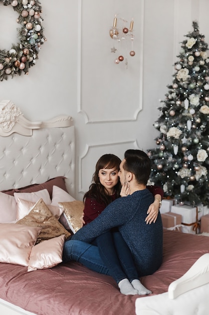 Lief paar knuffelen op het bed in een slaapkamer ingericht voor kerstvakantie