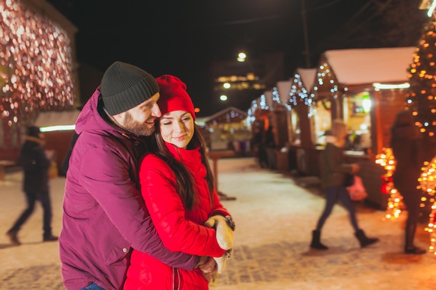 Lief romantisch verliefd stel staat in nauwe omhelzing terwijl nieuwjaarsviering in het centrum, in de buurt van de kerstmarkt. Grote hoeveelheid lichten en verlichting op houten huizen op de achtergrond