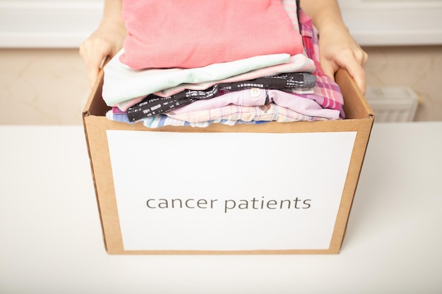 Liefdadigheid en hulp aan mensen in nood Vrouwenhanden houden een doos met kleding voor kankerpatiënten vast