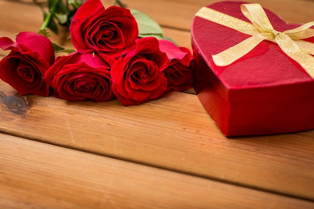 liefde, datum, romantiek, Valentijnsdag en feestdagen concept - close-up van hartvormige geschenkdoos en rode rozen op houten tafel
