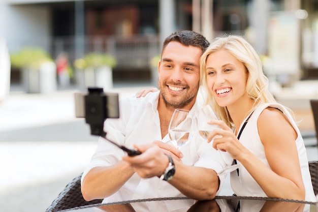 liefde, datum, technologie, mensen en vakantie concept - gelukkige gelukkige paar nemen foto met smartphone op selfie stick en rammelende bril in city street café of restaurant