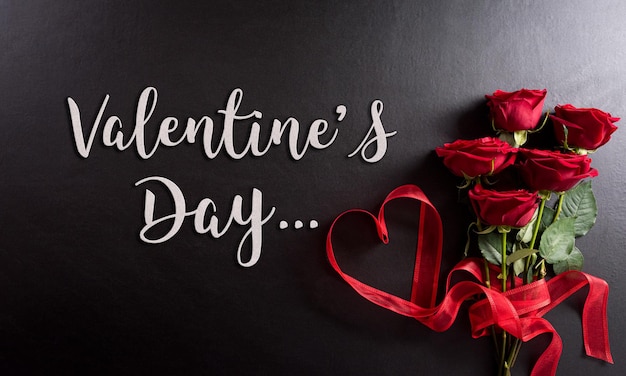Liefde en Valentijnsdag concept gemaakt van rode roos en hart lint met de tekst op zwarte houten achtergrond