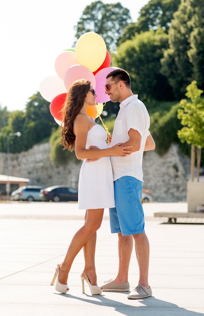 Liefde, huwelijk, zomer, dating en mensen concept - glimlachend paar dragen van een zonnebril met ballonnen knuffelen en kijken naar elkaar in het park