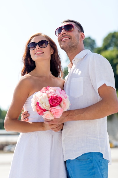 liefde, huwelijk, zomer, dating en mensen concept - glimlachend paar met zonnebril met bos bloemen knuffelen in de stad