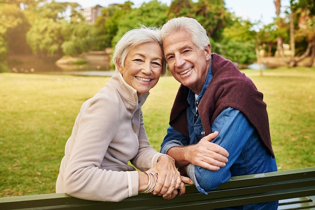 Liefde kent geen leeftijd Portret van een gelukkig senior koppel zittend op een bankje in het park