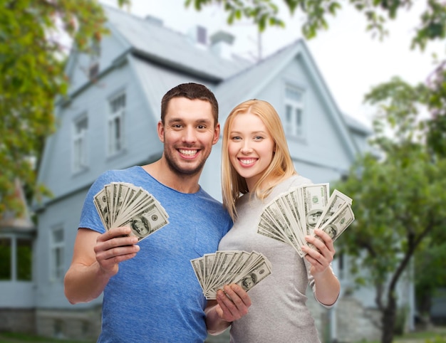 liefde, mensen, onroerend goed, huis en familieconcept - glimlachend paar dat dollarcontant geld over huisachtergrond toont
