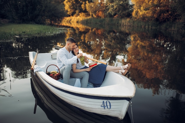 Liefde paar met fruitmand liggend in een boot op rustig meer op zomerdag. romantische ontmoeting, boottocht, man en vrouw wandelen langs de rivier