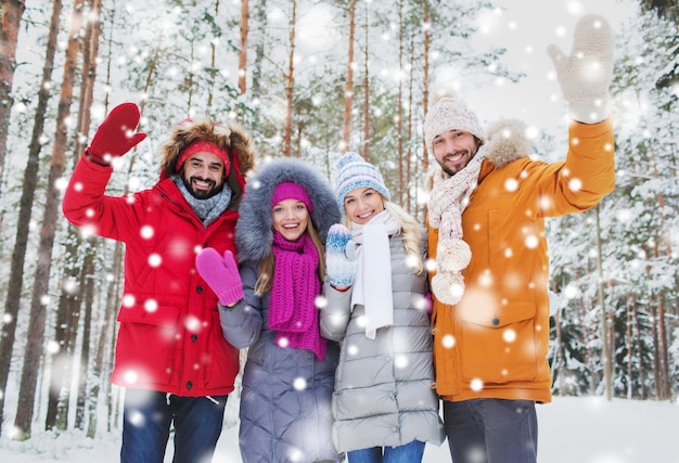 liefde, relatie, seizoen, vriendschap en mensenconcept - groep glimlachende mannen en vrouwen die handen zwaaien in het winterbos