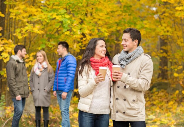 liefde, relatie, seizoen, vriendschap en mensenconcept - groep glimlachende mannen en vrouwen die met papieren koffiekopjes lopen in het herfstpark