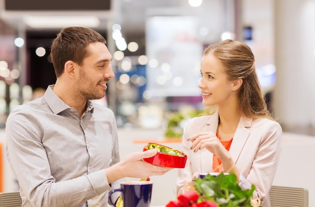 Liefde, romantiek, valentijnsdag, paar en mensen concept - gelukkig jong stel met rode bloemen en open geschenkdoos in café mall