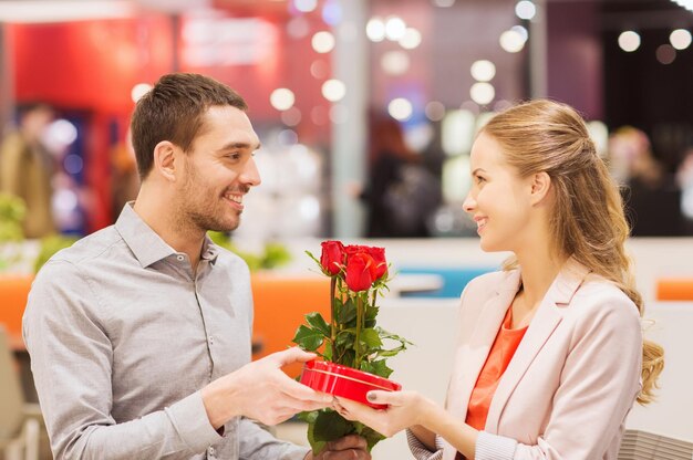 liefde, romantiek, Valentijnsdag, paar en mensen concept - gelukkige jonge man met rode bloemen cadeau geven aan lachende vrouw in café in winkelcentrum