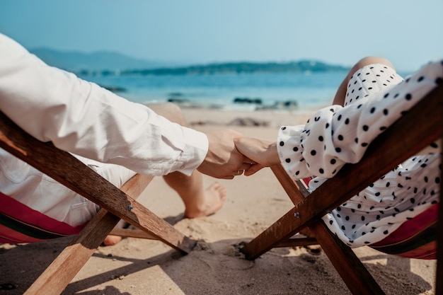 Liefde - romantische paarholdingshanden op een strand in zonsondergang terwijl sittinlanterfanters