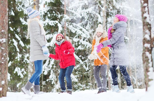 liefde, seizoen, vriendschap, entertainment en mensenconcept - groep gelukkige mannen en vrouwen die plezier hebben en sneeuwballen spelen in het winterbos